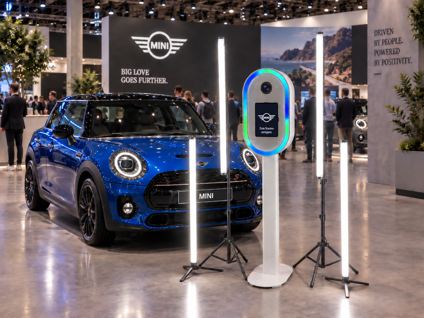 KI-Fotobox mit MINI-Branding, Kamera, Touchscreen und Licht neben einem blauen MINI auf einem Messestand · Konzeptvisualisierung